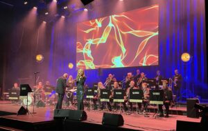Stavanger Storband i konsert på scene med fargerikt lerret i bakgrunnen.