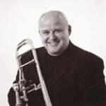 Svart/hvitt bilde av PK Svensen, trombonist og professor, lener trombonen sin på høyre skulder.