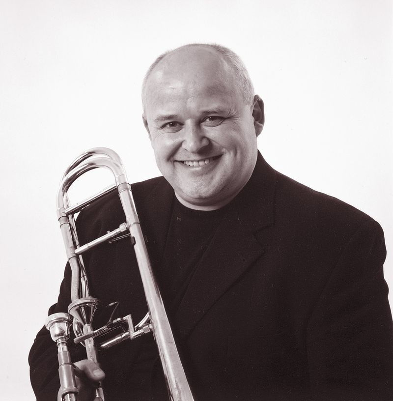 Svart/hvitt bilde av PK Svensen, trombonist og professor, lener trombonen sin på høyre skulder.